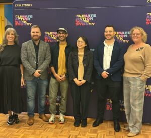 Six people of different heights in a row in front of a purple background with the text "Climate Action Week Sydney" printed on it